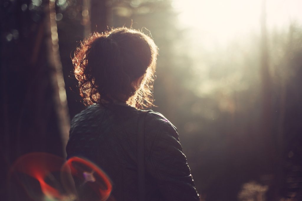 Woman looking into forest with sun shining on her