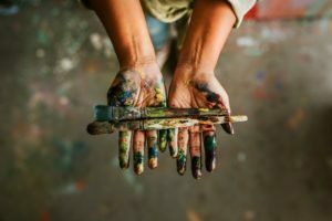 Hands holding paint brush, covered in paint