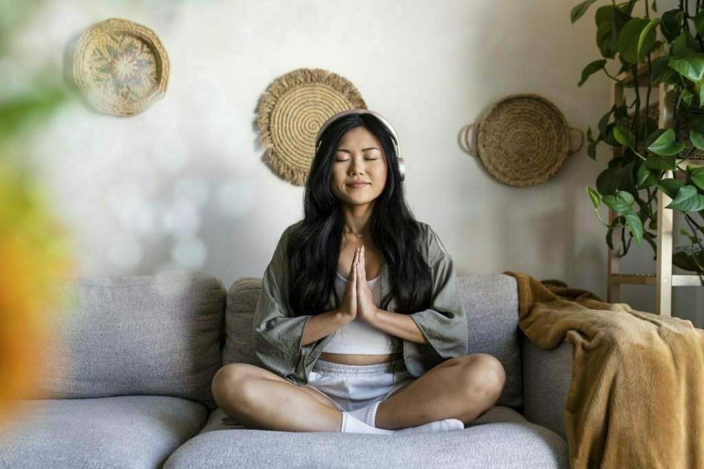An asian woman listening to music and meditating at home