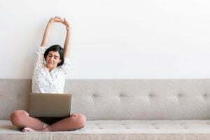 A woman stretching at her computer on the couch