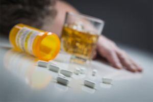 prescription drugs spilled on a table with an alcoholic beverage in the background